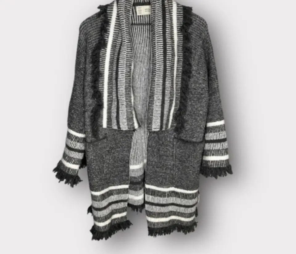 Cardigan largo de tejido grueso en tonos grises y blanco, con detalles de flecos en los bordes. Ideal para un look casual y abrigado.