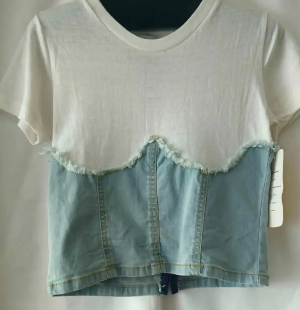 Remera de mujer con diseño de top de jean en la parte inferior. Corte en la cintura con detalle desflecado. Ideal para un look casual y moderno.