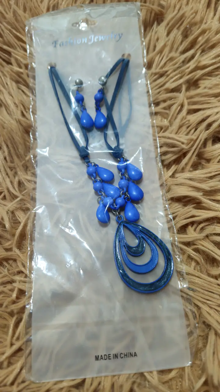 Conjunto de collar y aros de bisutería azul, ideal para darle un toque de color y estilo a cualquier look. El collar presenta un diseño con colgantes en forma de gotas y un dije central, mientras que los aros complementan el conjunto con un diseño a juego. Perfecto para ocasiones especiales o para realzar tu estilo diario.