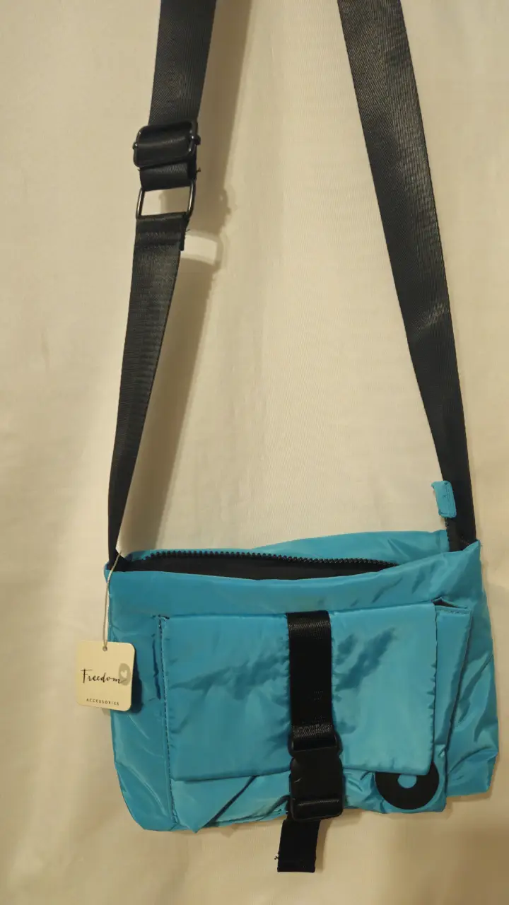 Bandolera de color celeste con detalles en negro. Cuenta con un bolsillo frontal y una correa ajustable. Ideal para llevar tus pertenencias de forma cómoda y segura. Medida 24*18 cm.
