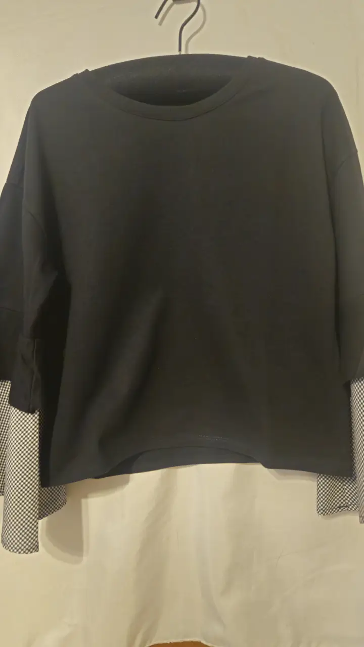 Buzo de cuello redondo negro con mangas en contraste de tela a cuadros blanco y negro. Ideal para un look casual y moderno.