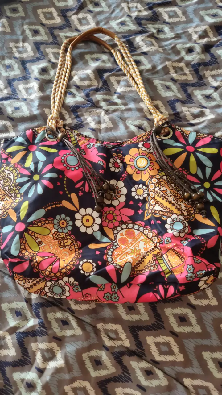 Bolso de playa con estampado floral vibrante. Diseño amplio y cómodo, ideal para llevar todo lo necesario para un día de sol. Asas trenzadas y detalles decorativos. Medida 42×30 × 10 cm