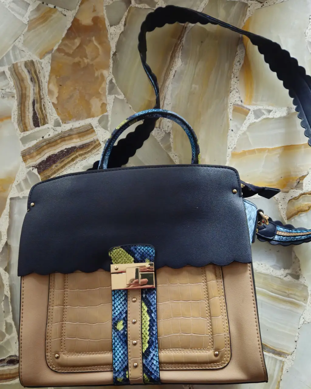Cartera de mano con diseño moderno, combinando azul y beige con detalles en azul y beige. Posee un cierre dorado y una correa para llevar al hombro. Medida 28*29*12 cm . Madera in Dubai.