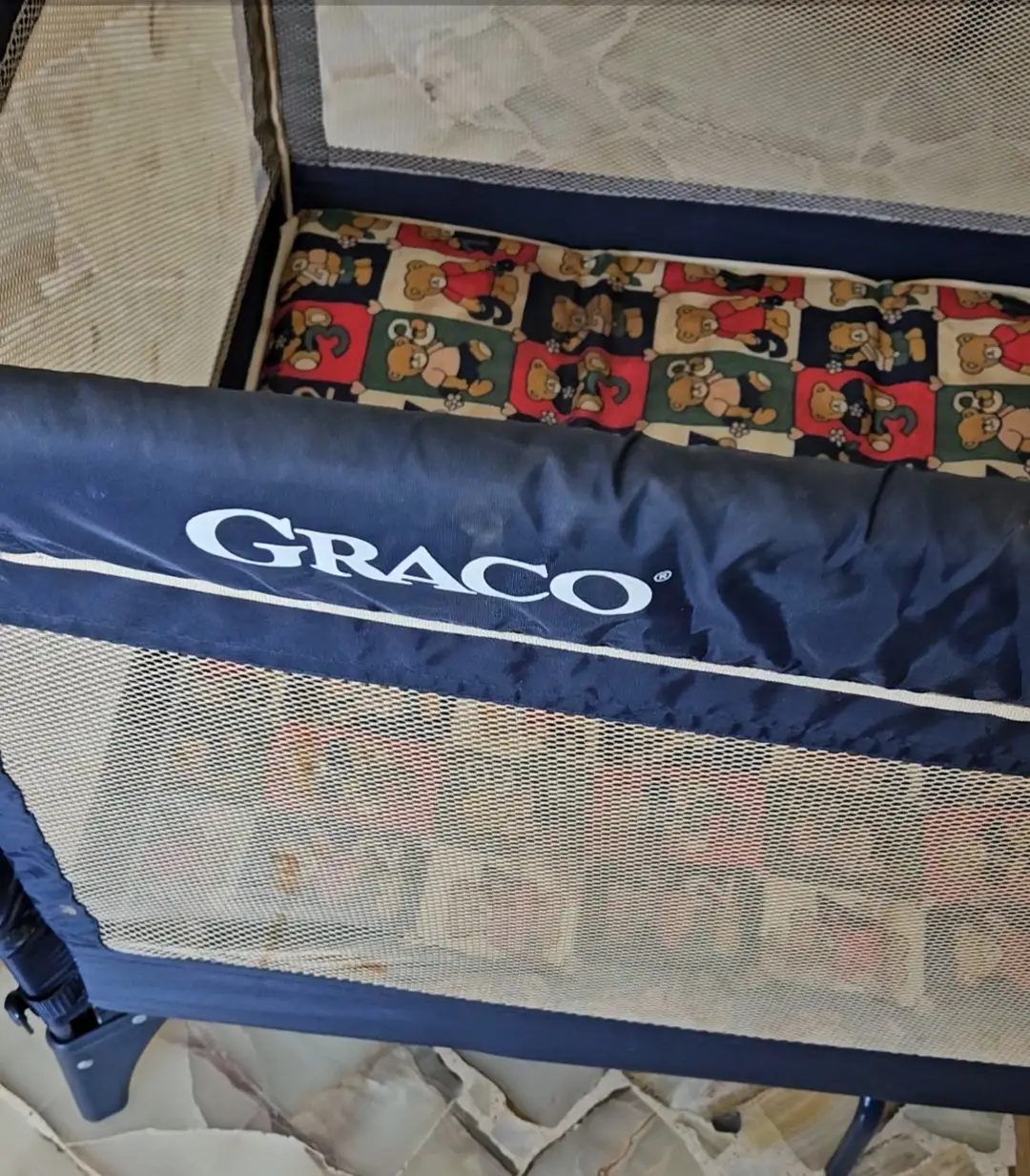 Cuna de viaje Graco Pack 'n Play, color azul marino con detalles blancos. Incluye colchón con estampado de ositos y laterales de malla para ventilación. Ideal para bebés y niños pequeños.