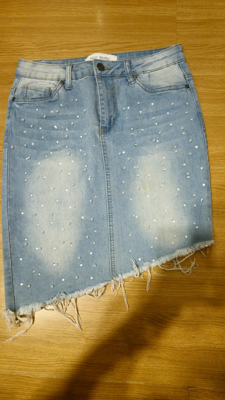 Minifalda de jean azul claro con detalles de strass. Corte asimétrico y desflecado en el borde inferior. Ideal para un look casual y moderno.