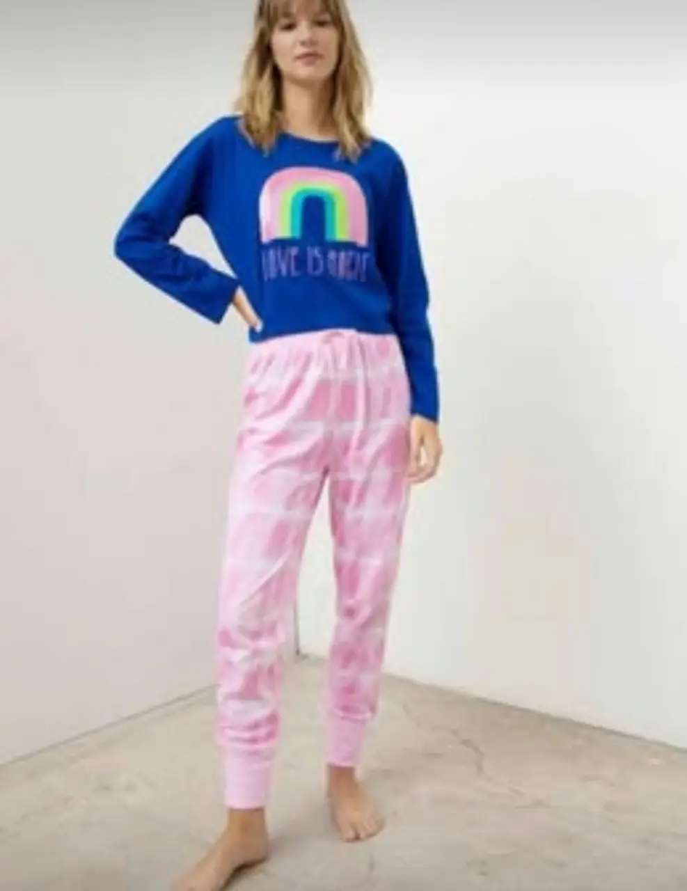 Pijama de dos piezas para mujer, con remera manga larga azul con estampado de arcoíris y frase. El pantalón es rosa con estampado a cuadros.