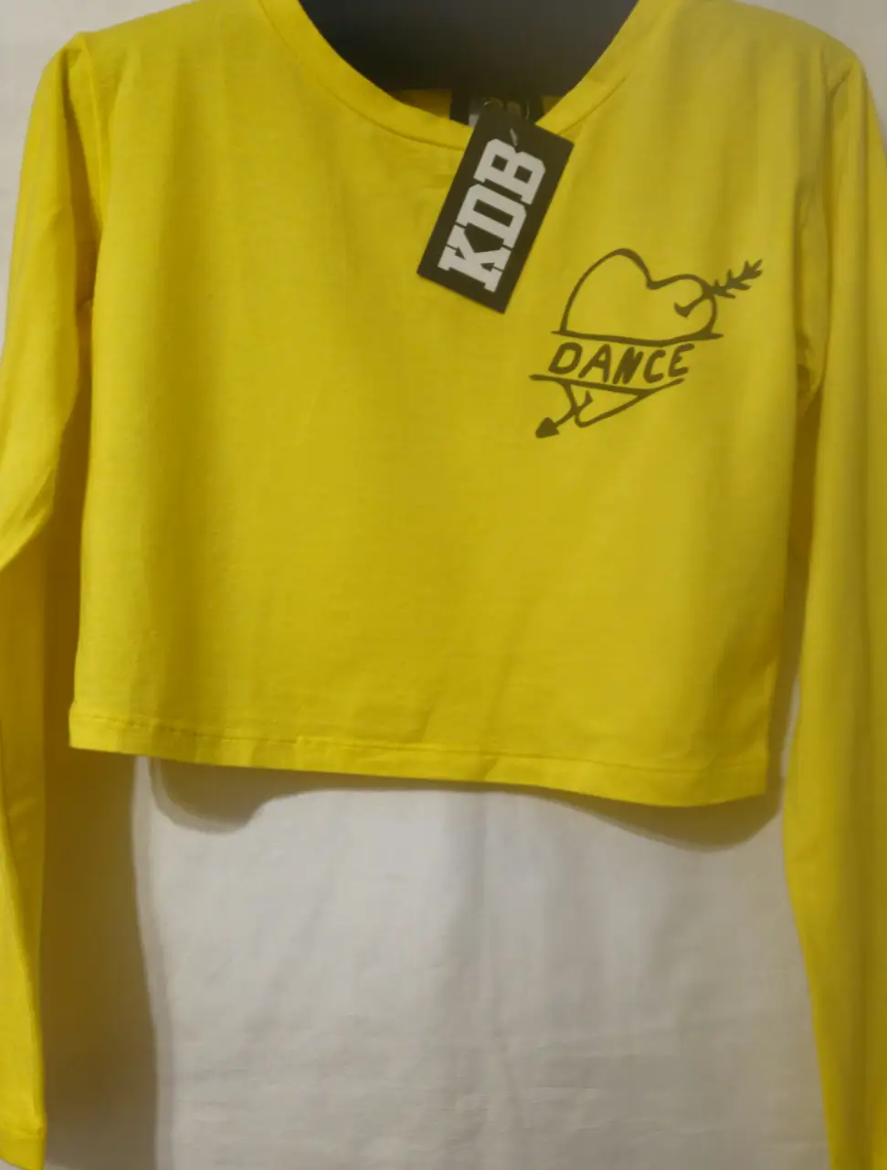 Remera manga larga crop de color amarillo con estampado de corazón y la palabra 'DANCE'. Ideal para un look casual y moderno.