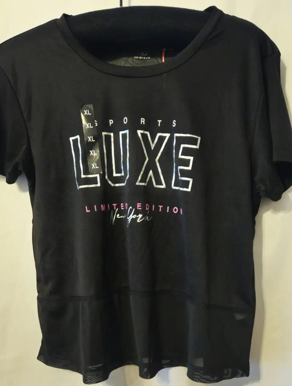 Remera deportiva negra de la marca K-Sport. Confeccionada con tejido técnico, presenta un diseño "LUXE" estampado en plateado y detalles en rosa. Ideal para actividades deportivas con un toque de estilo.