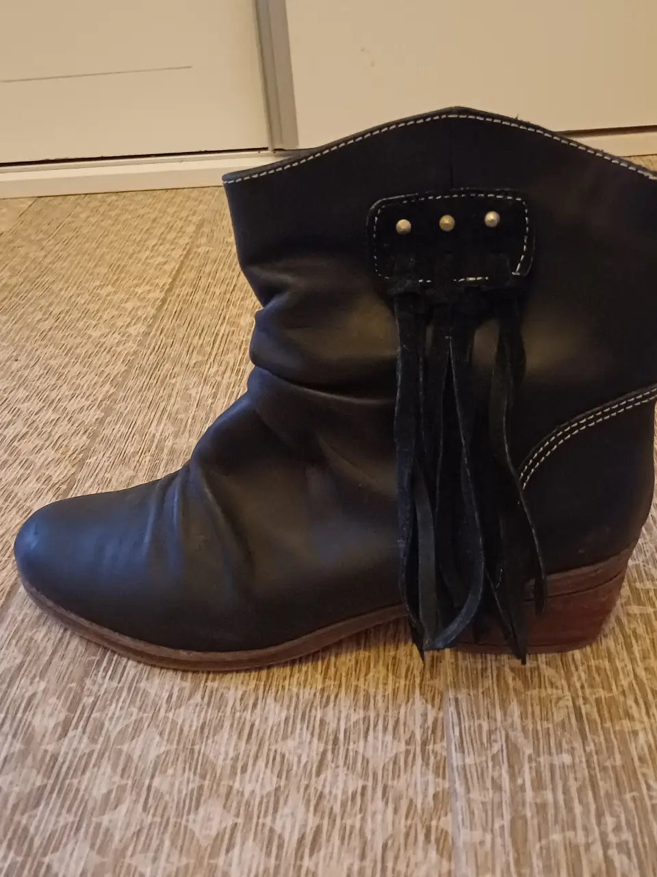 Botas negras de cuero con detalles de flecos y taco bajo. Ideales para un look casual y cómodo.