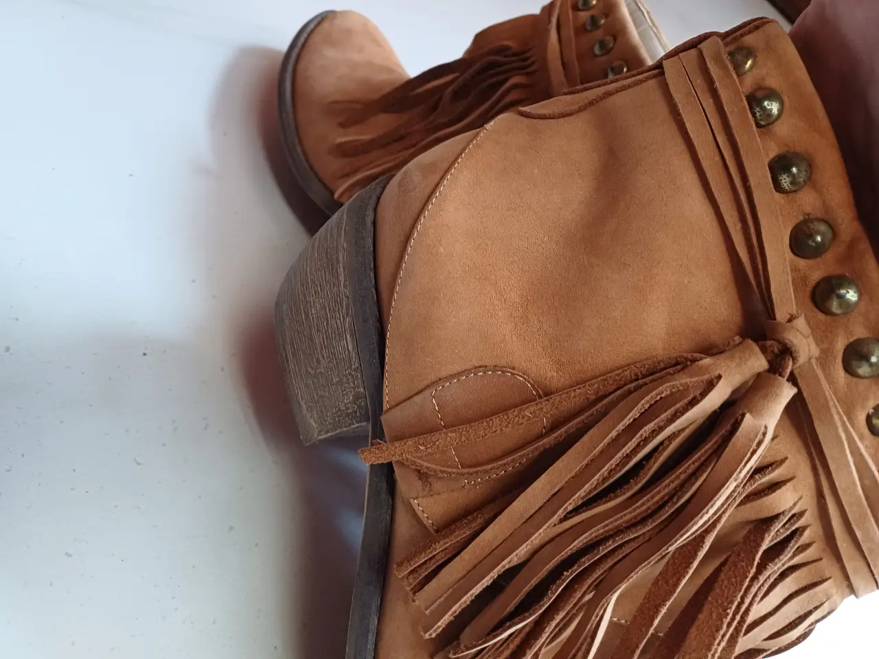 Botas de caña baja de gamuza marrón con flecos y detalles de tachas doradas. Estilo boho y artesanal, ideales para un look casual y con onda.