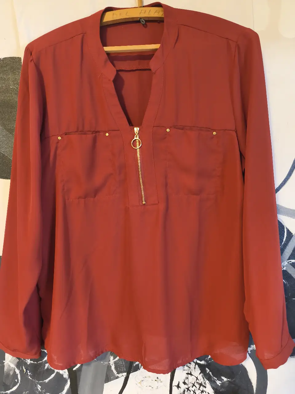 Blusa roja de manga larga con detalle de cierre dorado en el frente y bolsillos. Ideal para un look elegante y versátil.
