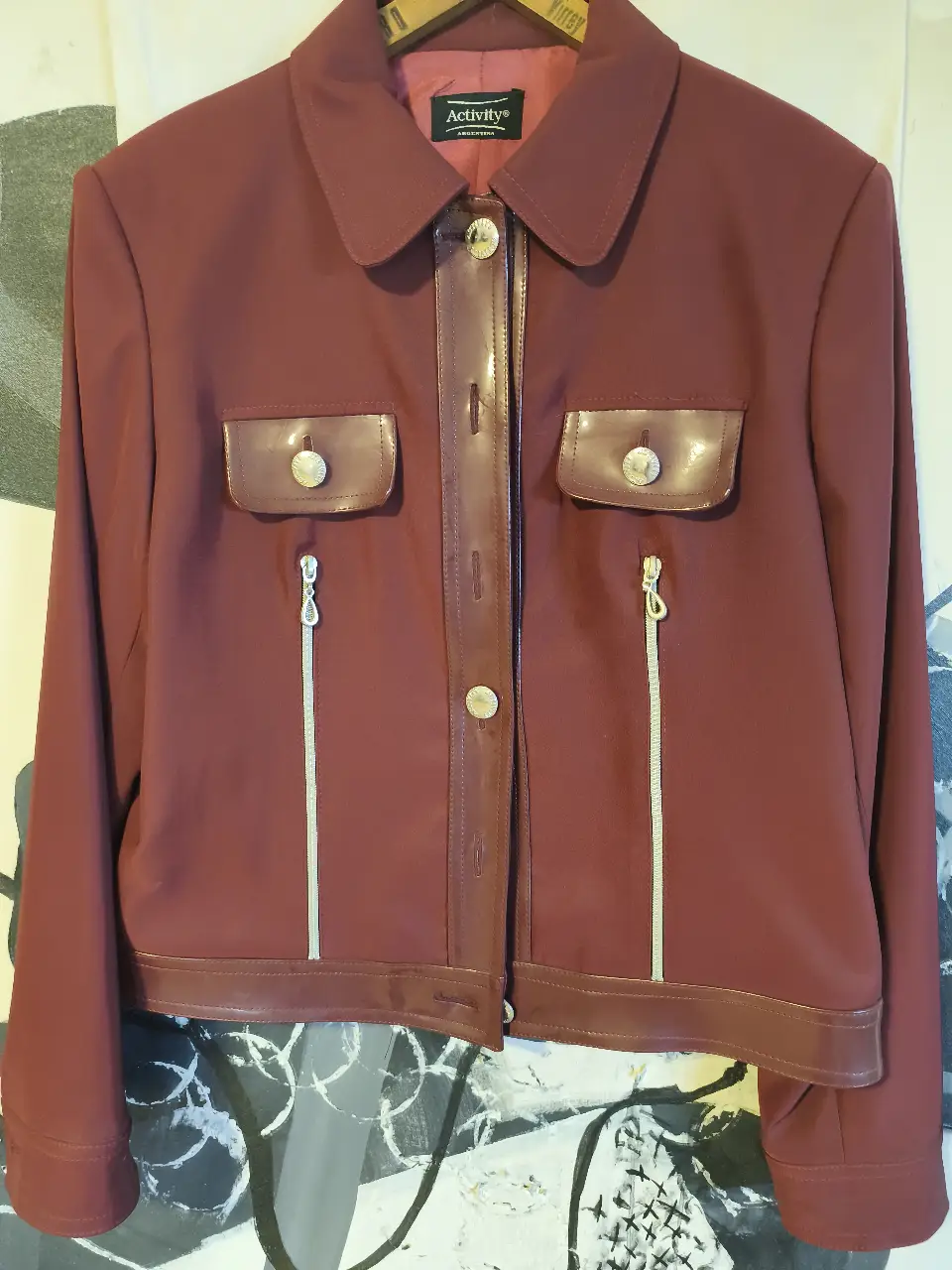 Chaqueta de mujer color borgoña con detalles de cierres . Posee dos bolsillos con solapa y cierre. Ideal para un look elegante y sofisticado.