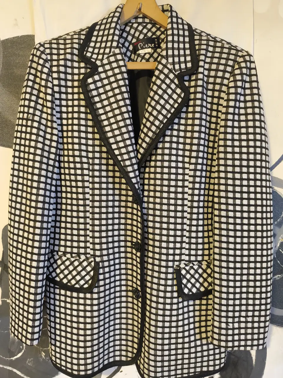 Elegante blazer de mujer con estampado a cuadros en blanco y negro. Diseño clásico con solapas, bolsillos y detalles en negro. Ideal para un look sofisticado y versátil.