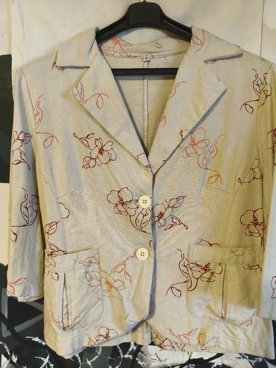 Blazer de mujer con estampado floral en tonos crudo y rojo. Corte clásico con dos botones y bolsillos delanteros. Ideal para un look elegante y primaveral.