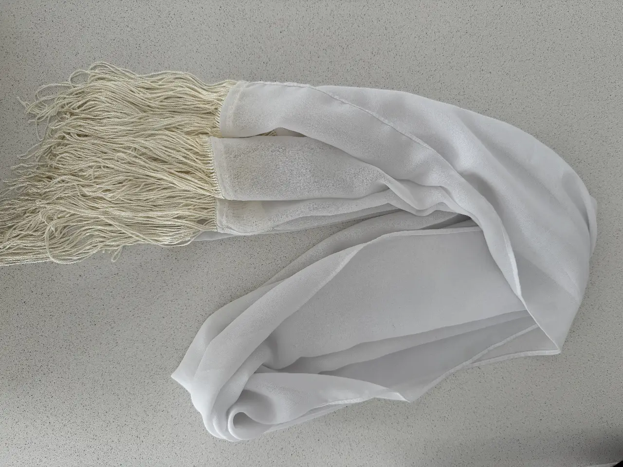 Pañuelo blanco con flecos, ideal para complementar cualquier look. Perfecto para ocasiones especiales o para darle un toque elegante a tu outfit diario. Le falta la etiqueta 