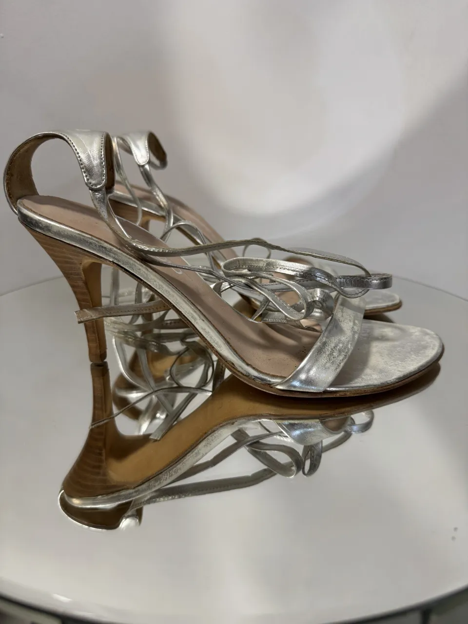 Sandalias Paruolo,  plateadas con tiras finas y taco alto. Las tiras se anudan alrededor del tobillo.
