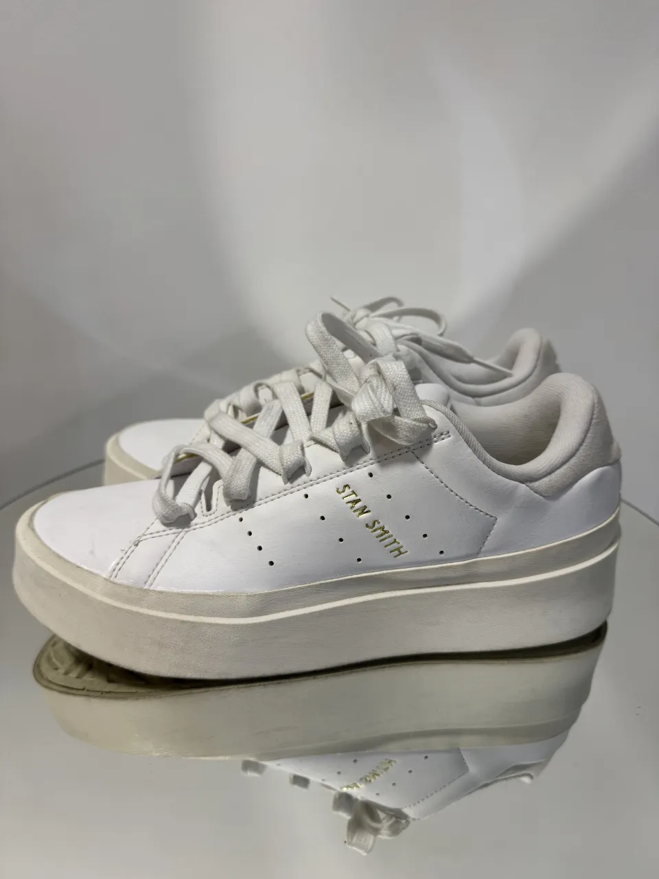Zapatillas Adidas, blancas de cuero con plataforma. Tienen cordones blancos y detalles dorados con el nombre de la marca. Impecables. 