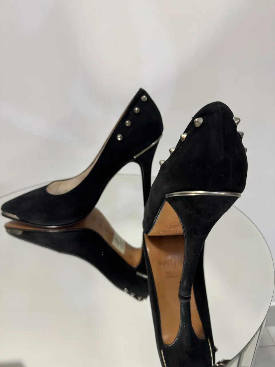 Zapatos de taco alto negros, estilo stiletto, con detalles de tachas plateadas en el borde superior y puntera metálica plateada. La marca 'Las Oreiro' se lee en la plantilla.