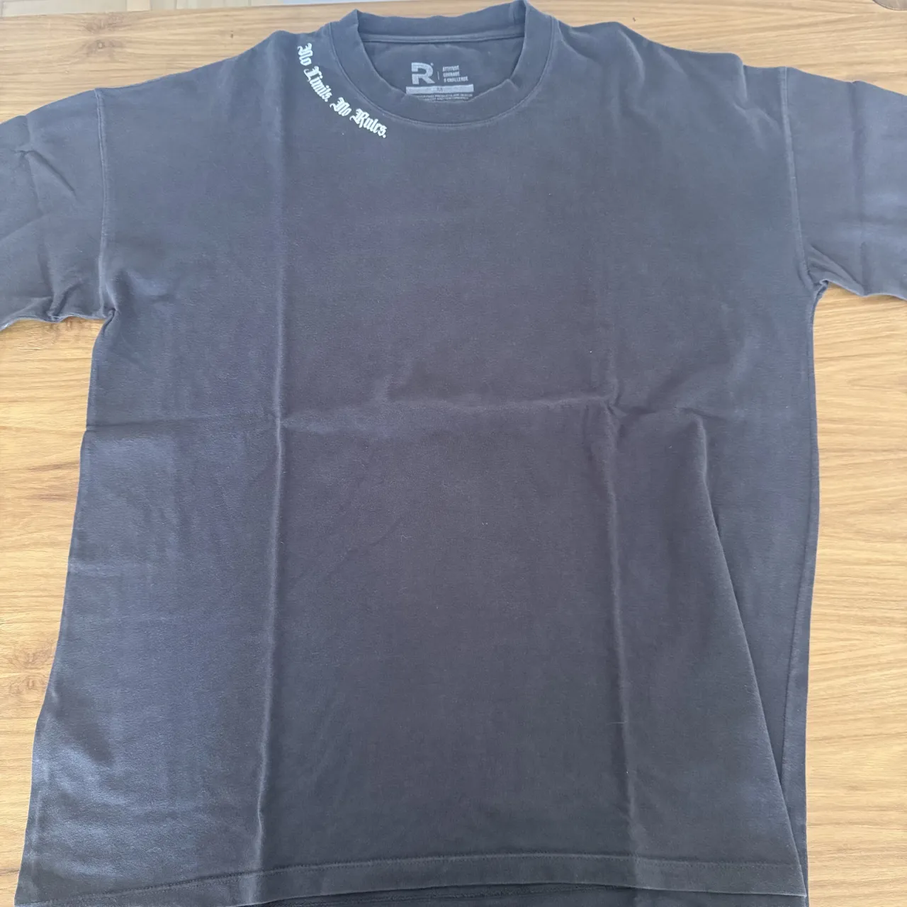 Remera REVER PASS gris oscura con estampa blanca en la espalda que dice "No Fears" en tipografía gótica. Debajo de la estampa principal, se lee "IF YOU HAVE NO FEARS, NO ONE HAS POWER OVER YOU" y un logo con la letra R.