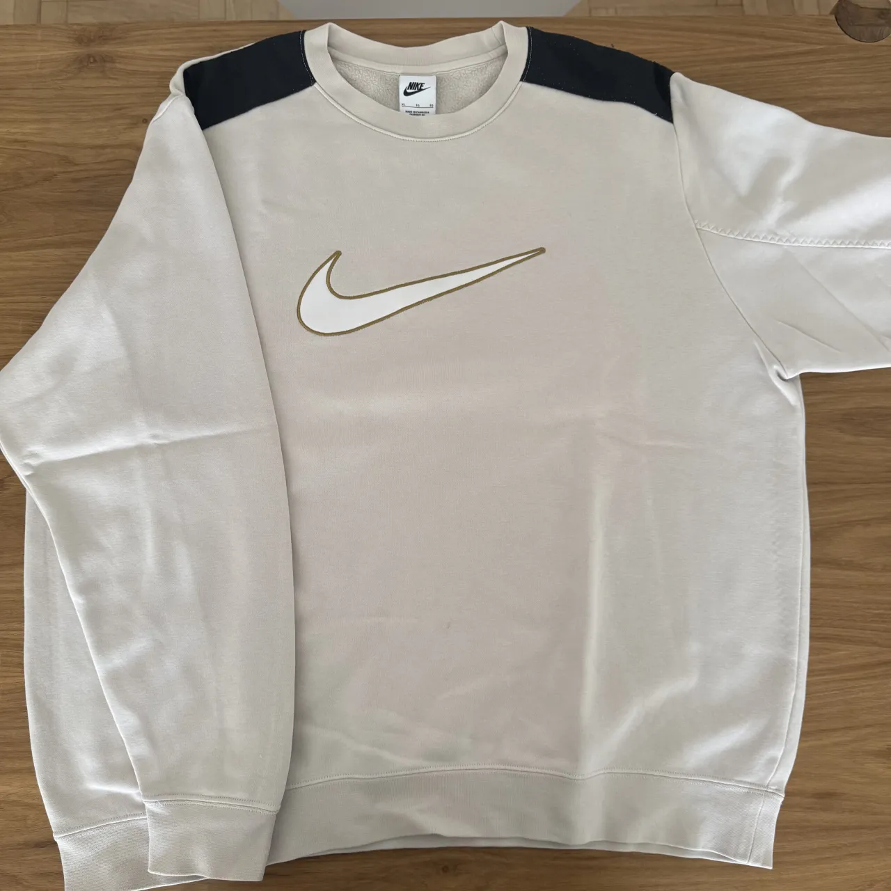 Buzo de algodón color crudo con logo de Nike bordado en el frente. Posee detalles en color negro en los hombros.