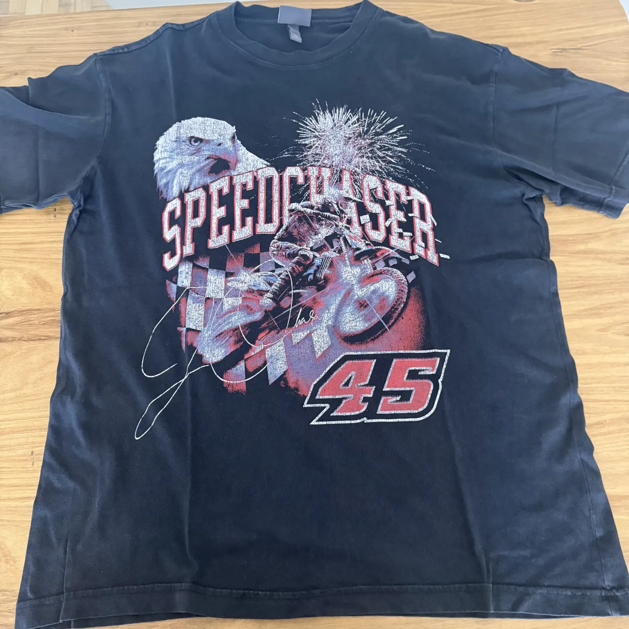 Remera H&M negra con estampa de un águila, una moto y fuegos artificiales. La estampa dice "SPEEDCHASER" y el número "45".