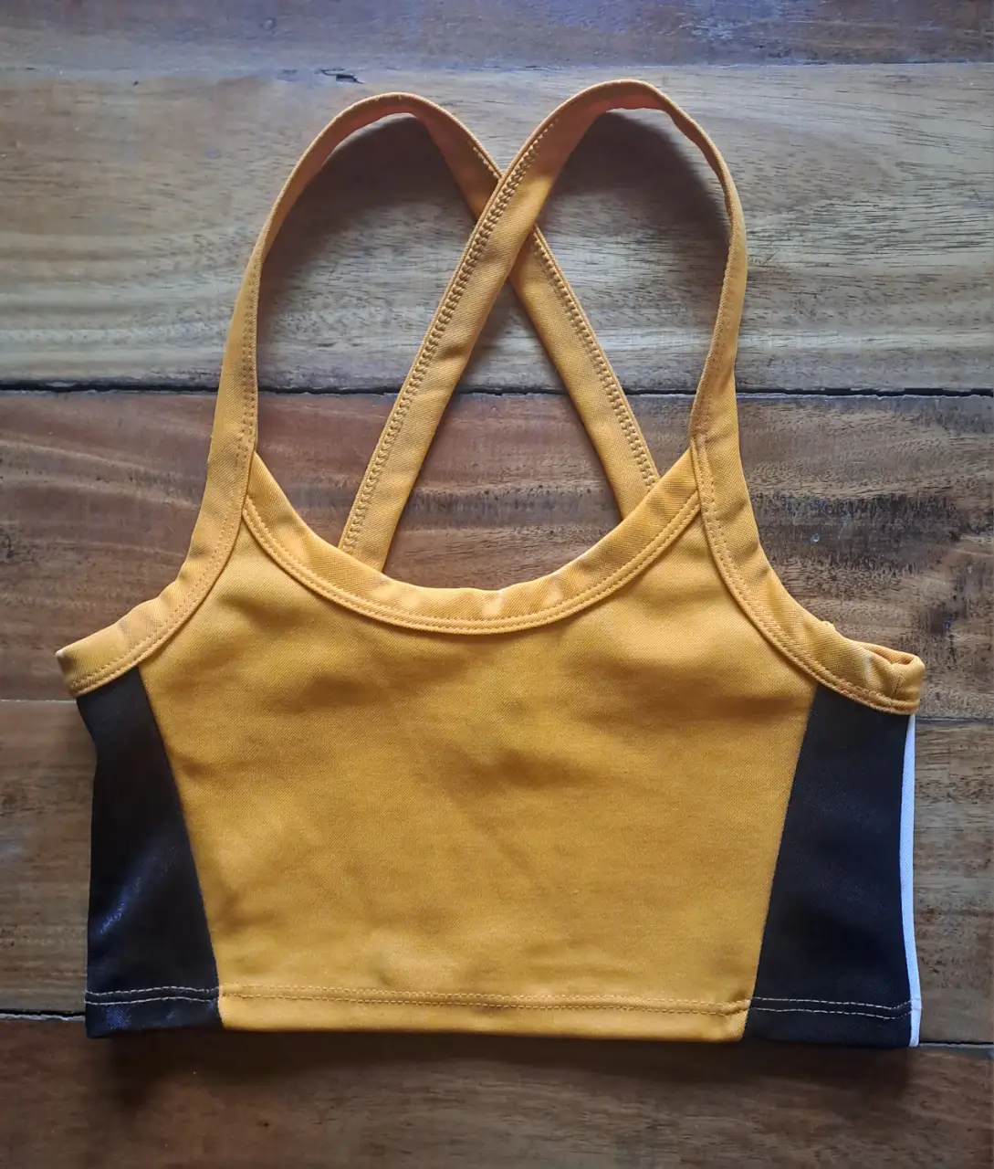 Top deportivo con diseño cruzado en la espalda, ideal para entrenamientos. Combina amarillo vibrante con detalles en negro y blanco. Marca NAF.