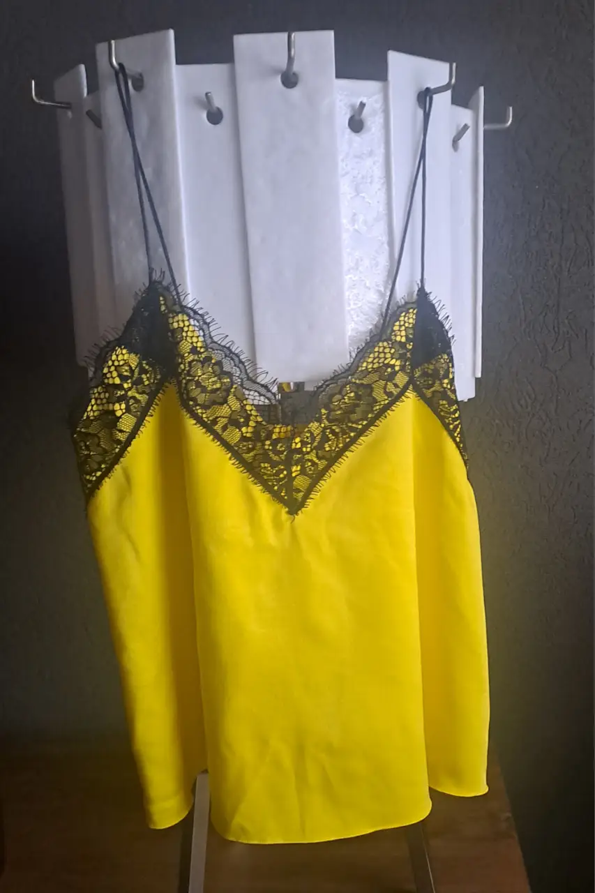 Top de seda amarillo con detalles de encaje negro en el escote y tirantes finos. Ideal para una salida o fiesta.
