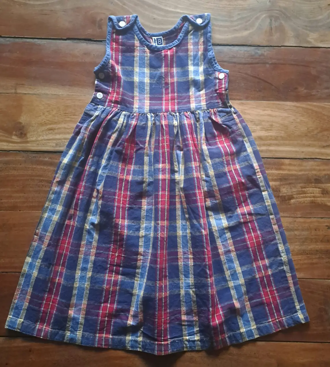 Vestido de niña a cuadrille. Diseño sin mangas, con botones decorativos en los hombros y detalle de fruncido en la cintura. 