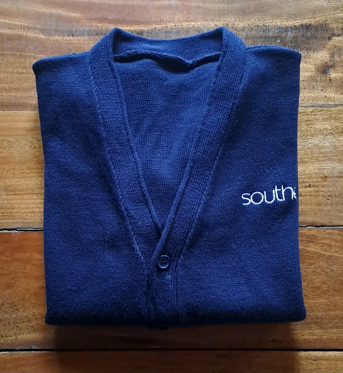 Cardigan azul marino con cuello en V y botones. Tiene el logo "southex" bordado en blanco. Ideal para un look colegial o casual.