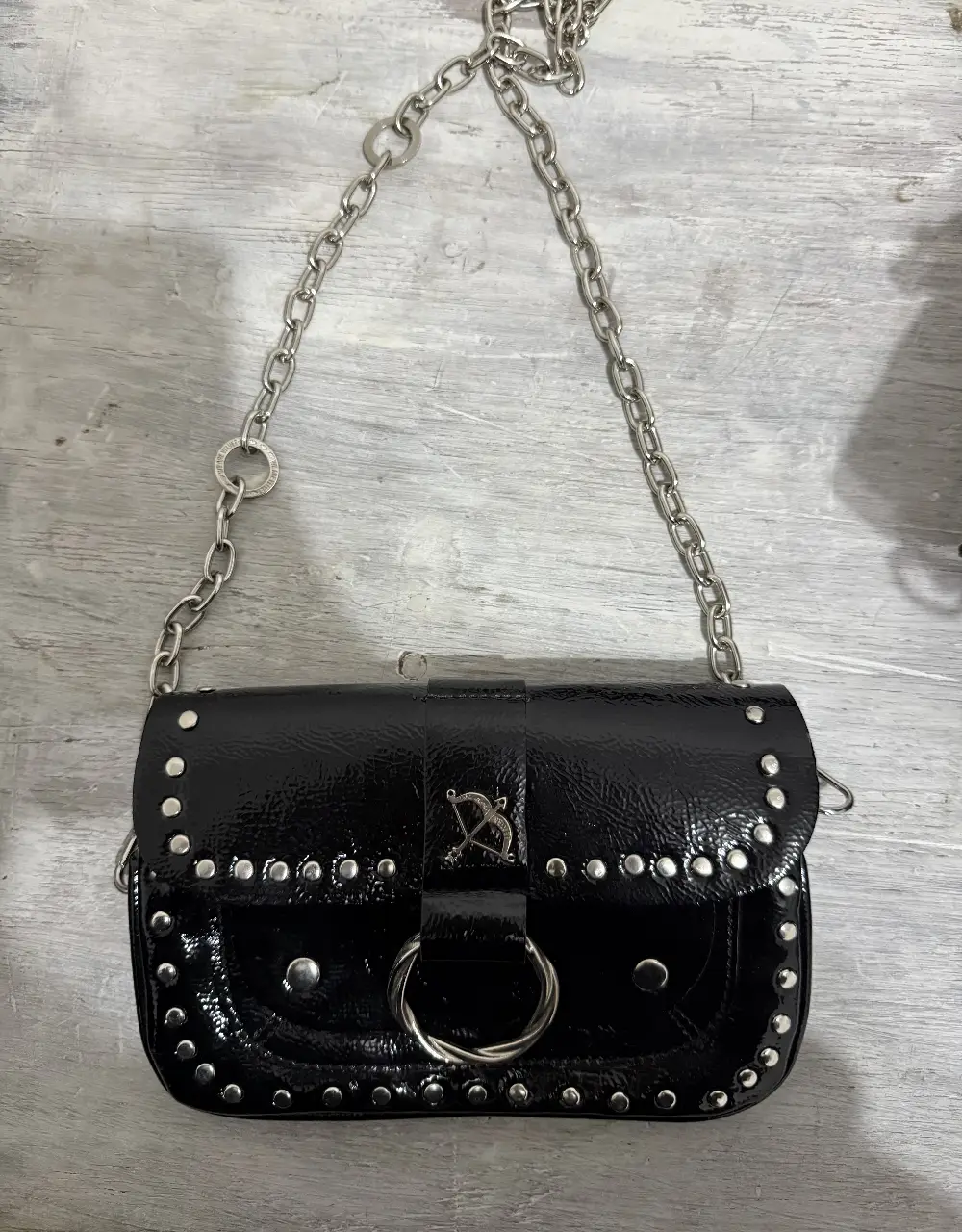 Cartera bandolera negra de charol con detalles de tachas y cadena plateada. Ideal para un look rocker y canchero.