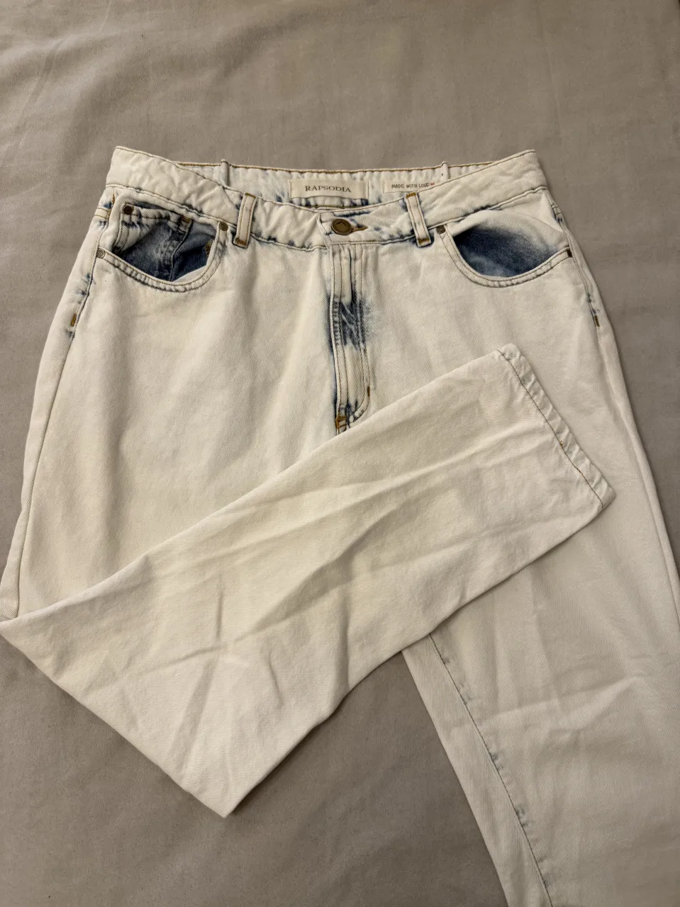 Jeans tiro alto, estilo mom, color blanco desgastado con detalles bordados en los bolsillos traseros. Un clásico reinventado para tu día a día.
