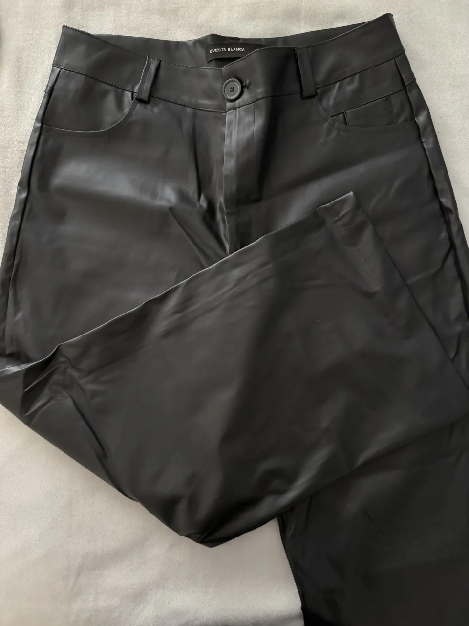 Pantalón negro de cuero sintético con botón y cierre.