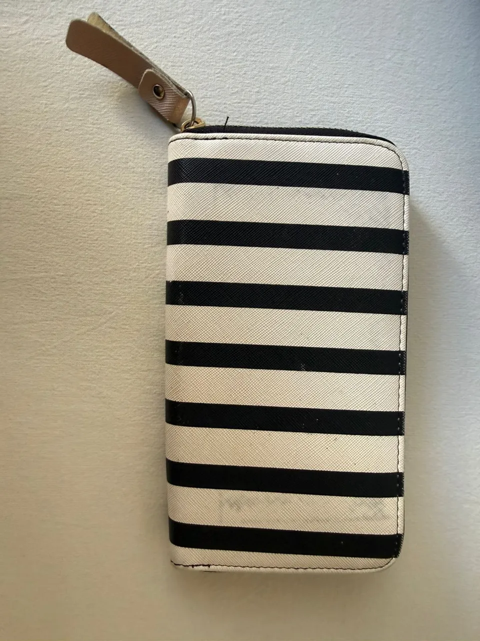 Billetera con cierre y estampa de rayas horizontales blancas y negras. Posee un detalle de tirador de cuero en uno de sus extremos.