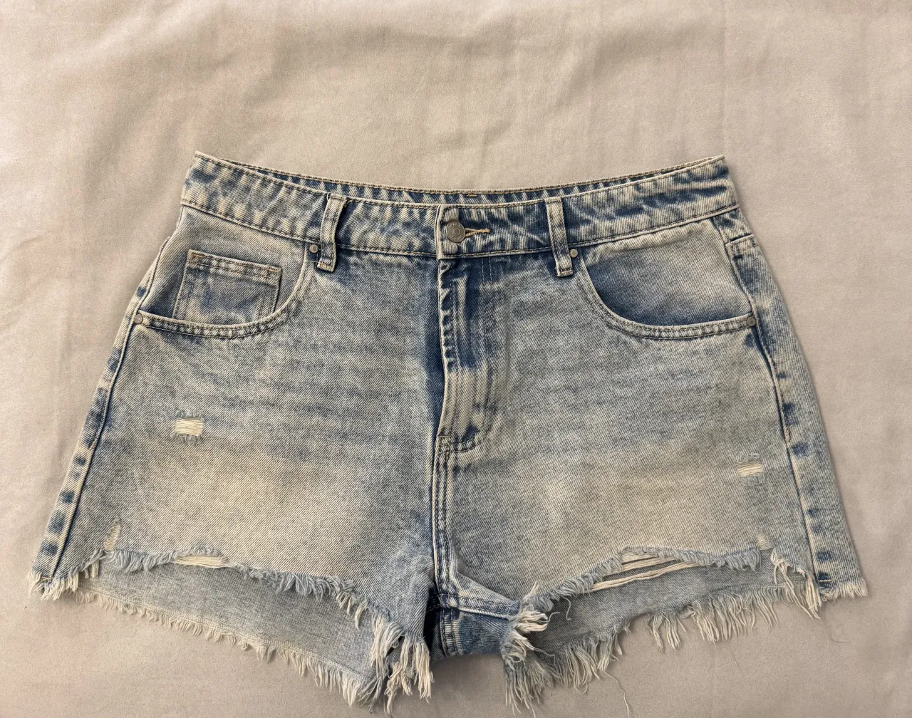 Shorts de jean tiro alto con roturas y detalles desflecados en el ruedo. Lavado desgastado y moderno, ideal para un look canchero y relajado.