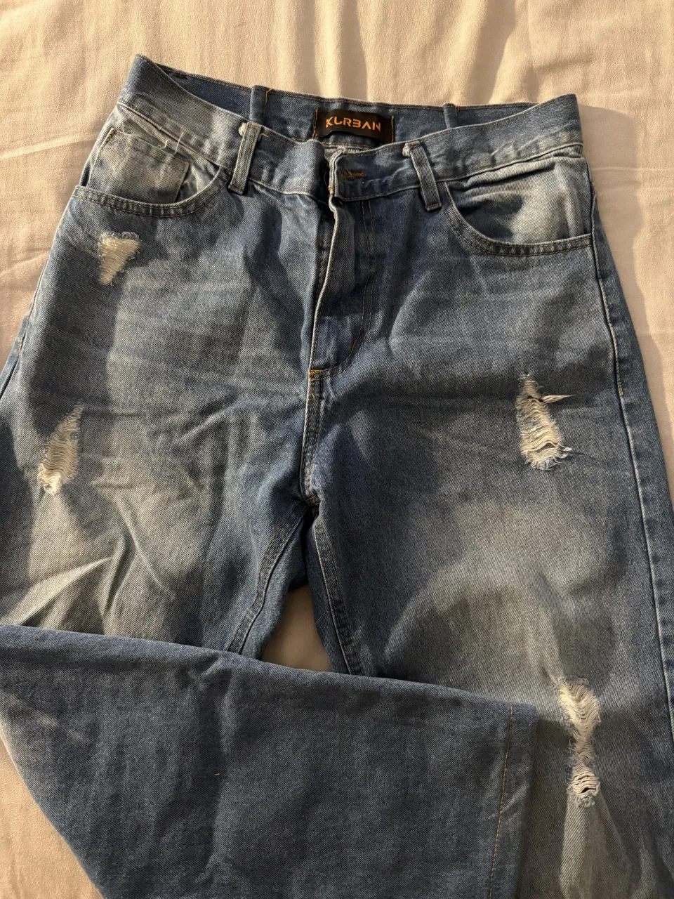 Jeans de denim azul con roturas y desgastes. Presenta bolsillos delanteros y traseros.