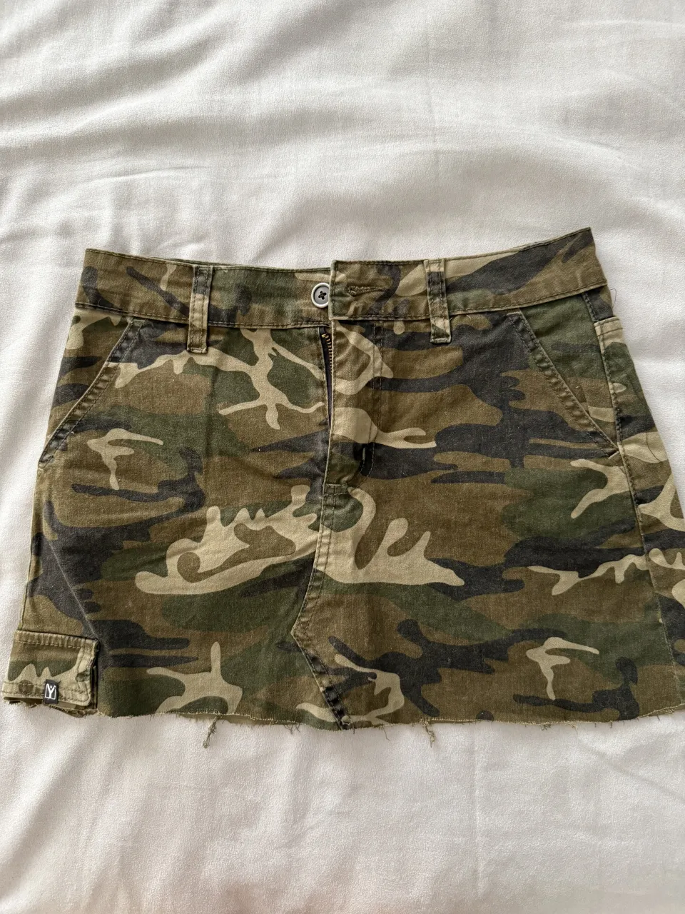 Pollera de jean tiro medio con estampa camuflada. Tiene bolsillos delanteros y traseros, y un detalle desflecado en el ruedo. Ideal para un look canchero y urbano.