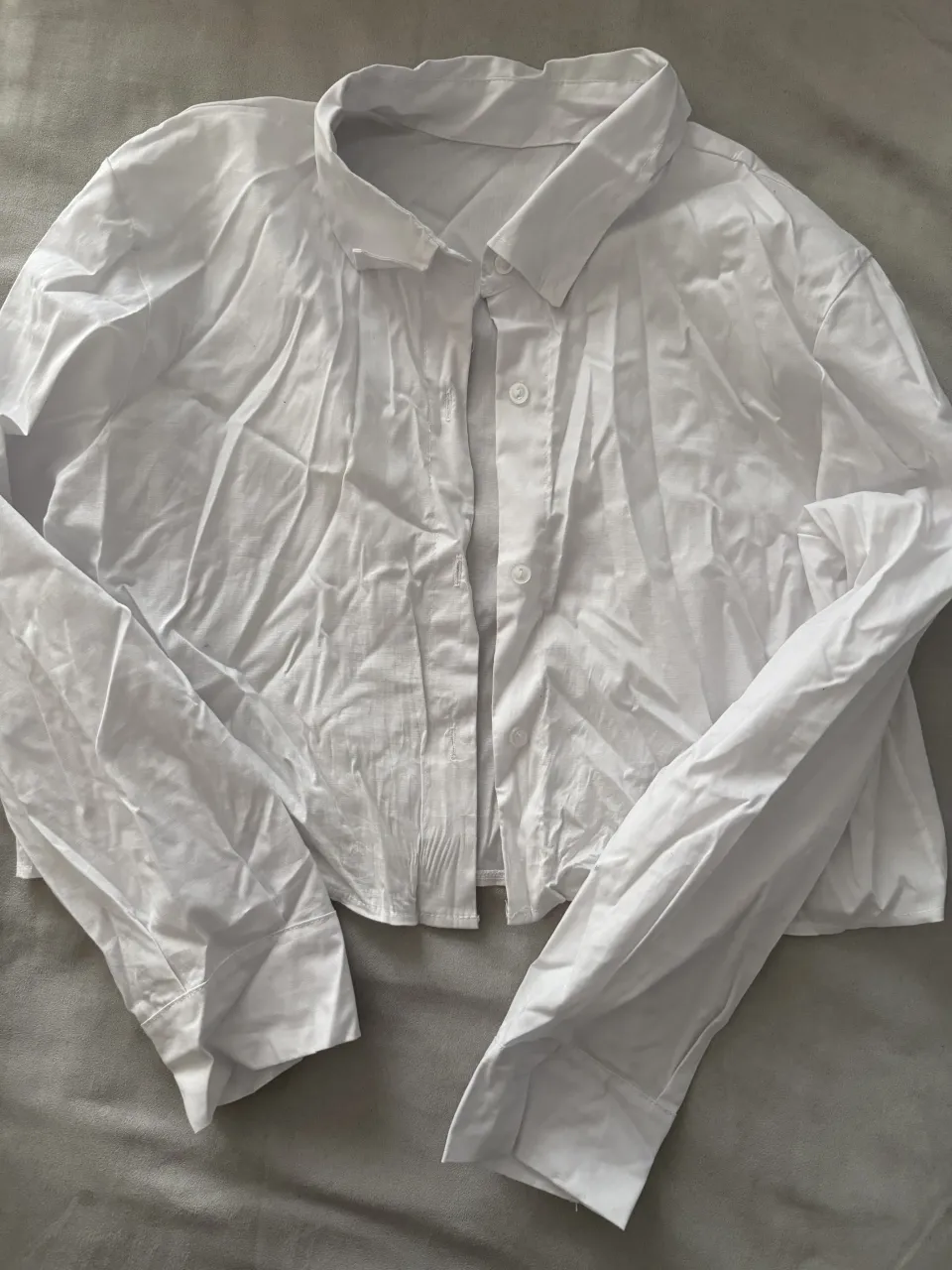 Camisa blanca de manga larga, con botones al frente y cuello. Es corta.