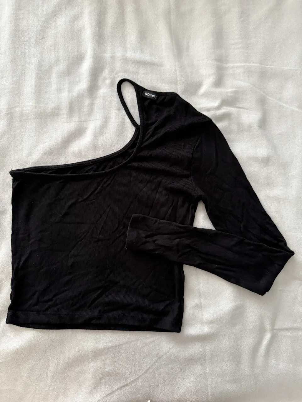 Remera negra de manga larga, con un solo hombro descubierto. Diseño ajustado y acanalado, ideal para un look moderno y canchero.