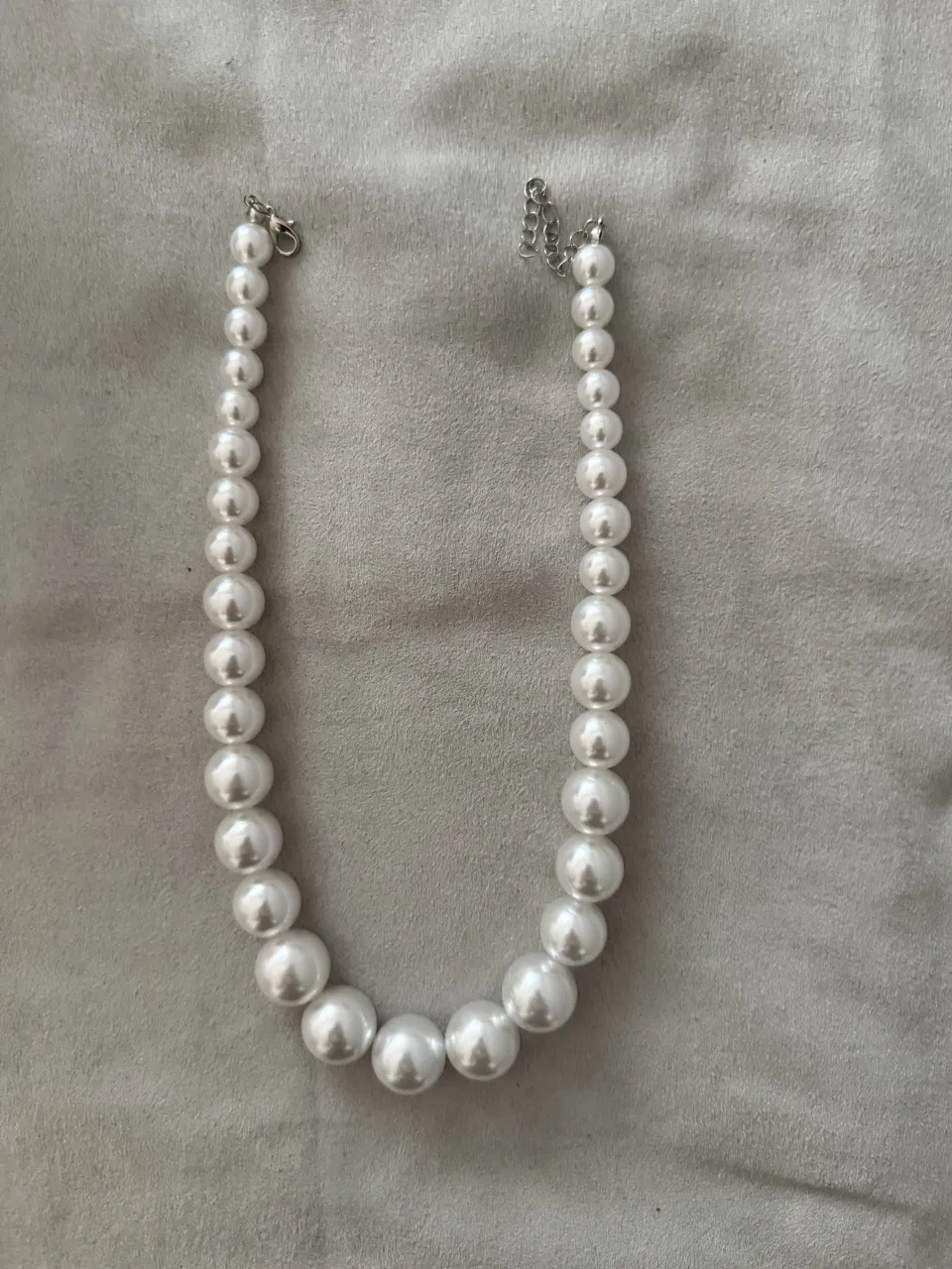 Collar de perlas blancas grandes con cadena plateada y cierre.