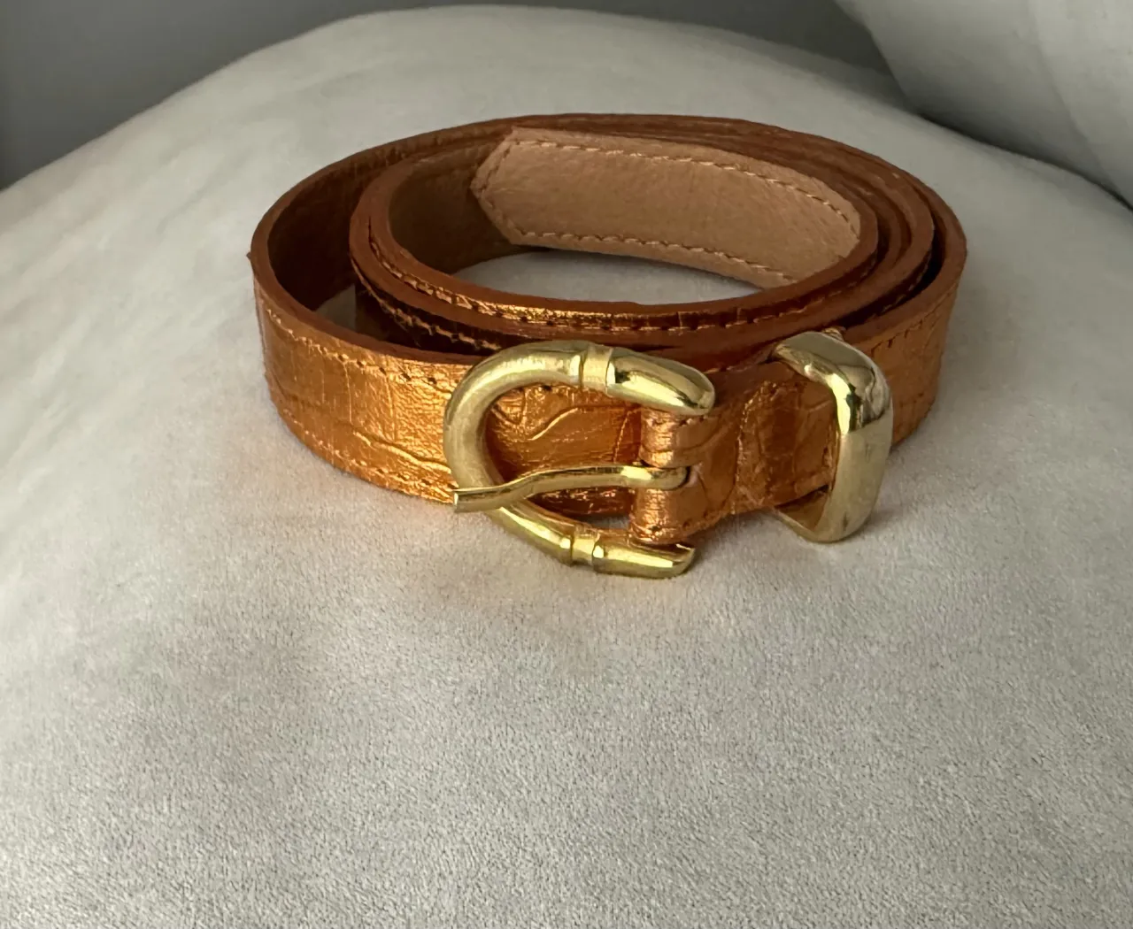 Cinturón de cuero sintético color dorado con hebilla dorada. Posee textura símil cocodrilo.