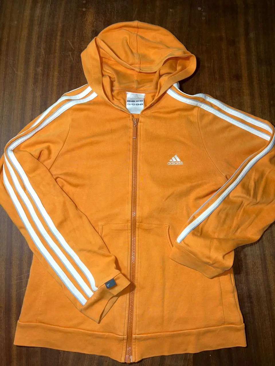 Buzo deportivo Adidas naranja con cierre y detalles blancos en las mangas. Ideal para actividades físicas o un look casual.