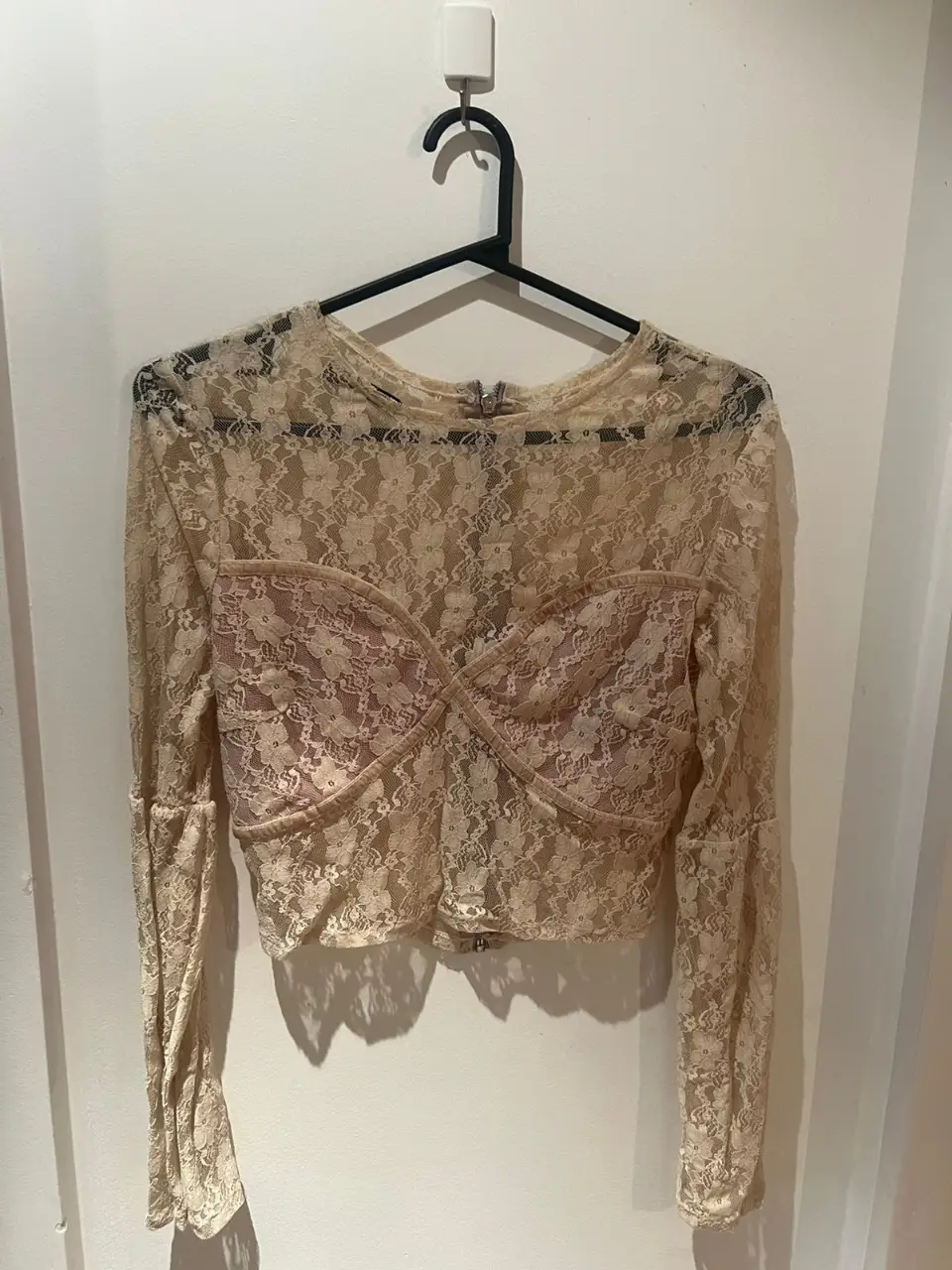 Blusa de encaje color crudo, con mangas largas y detalle de busto. Ideal para un look elegante y sofisticado.