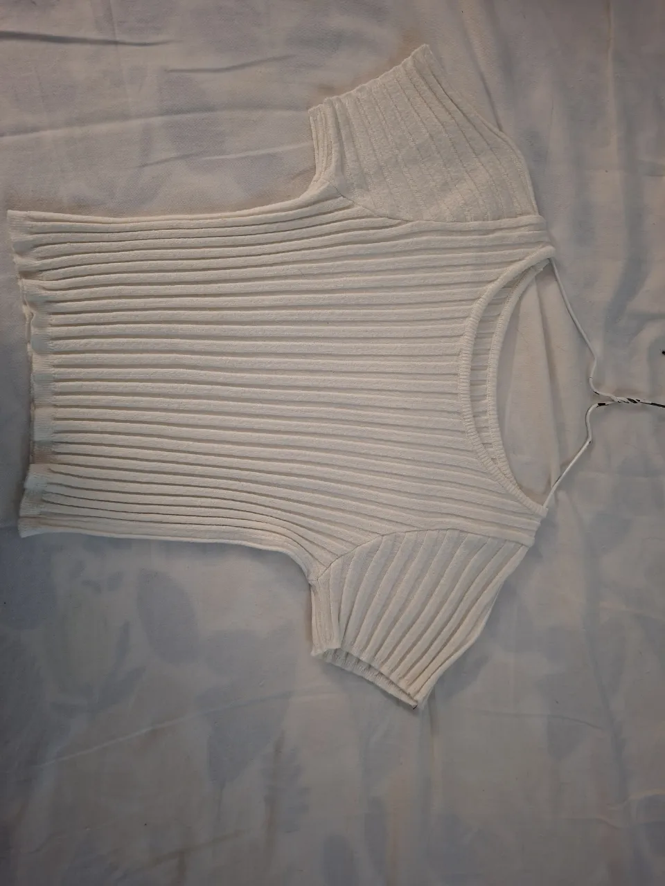 Top blanco de tejido acanalado, con mangas cortas y escote redondo. Ideal para un look casual y moderno.