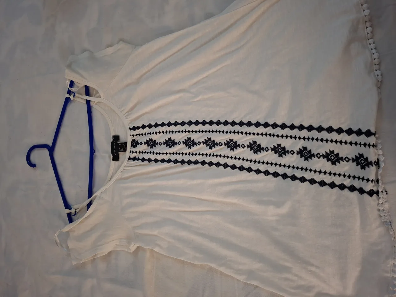 Remera blanca con detalles bordados en negro en el frente. Posee tiras finas en los hombros y un diseño tribal en el pecho. Ideal para un look casual y fresco.