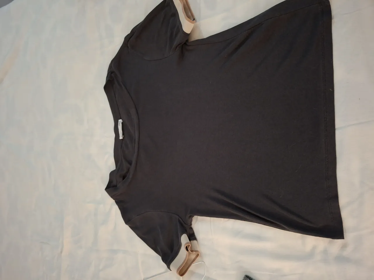 Remera manga corta de color gris oscuro, con detalles de franjas en los puños en color blanco y rosa pálido. Ideal para un look casual y cómodo.