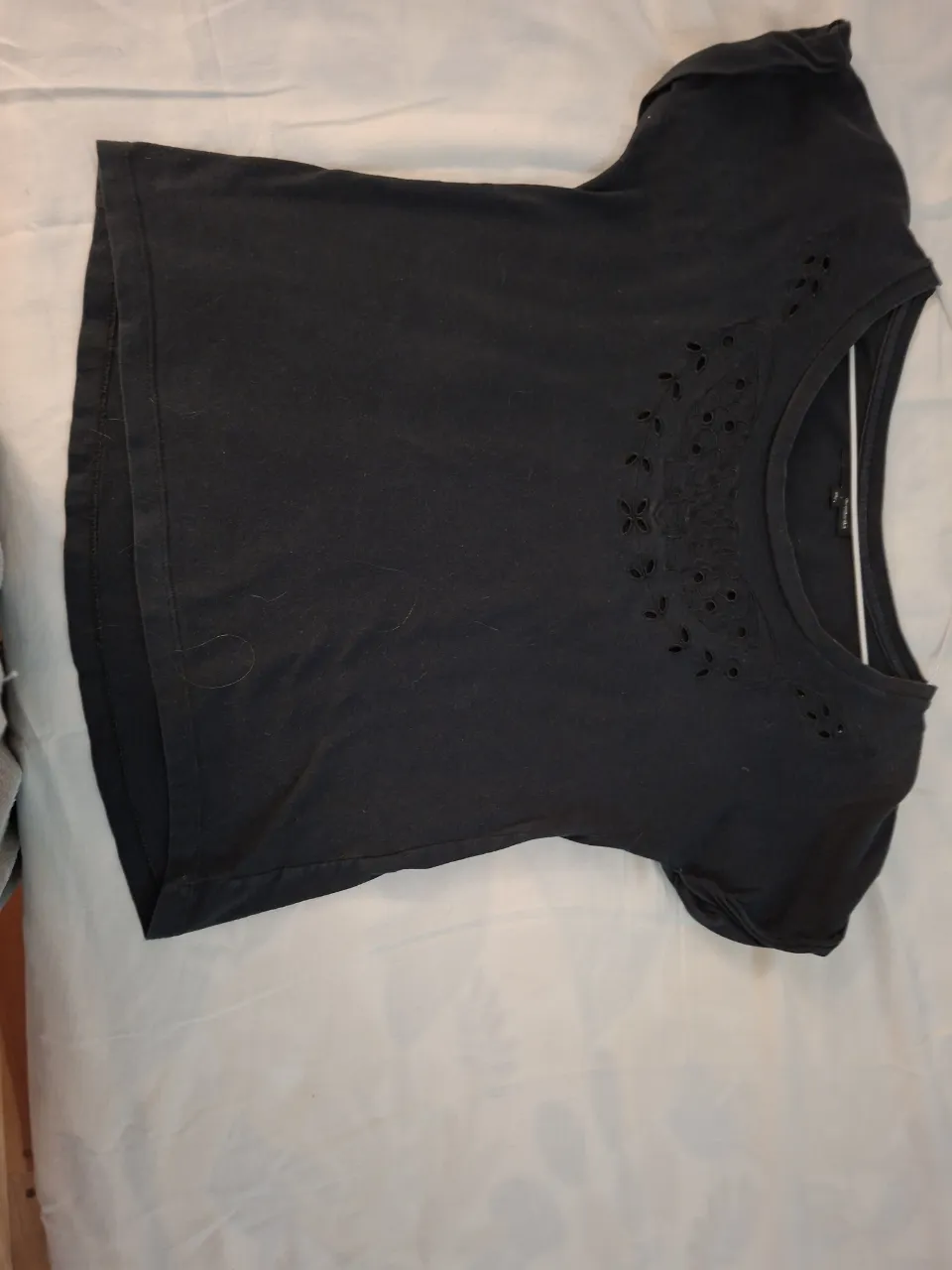 Remera negra con detalles bordados y calados en el cuello. Manga corta y escote redondo. Perfecta para un look casual y femenino.