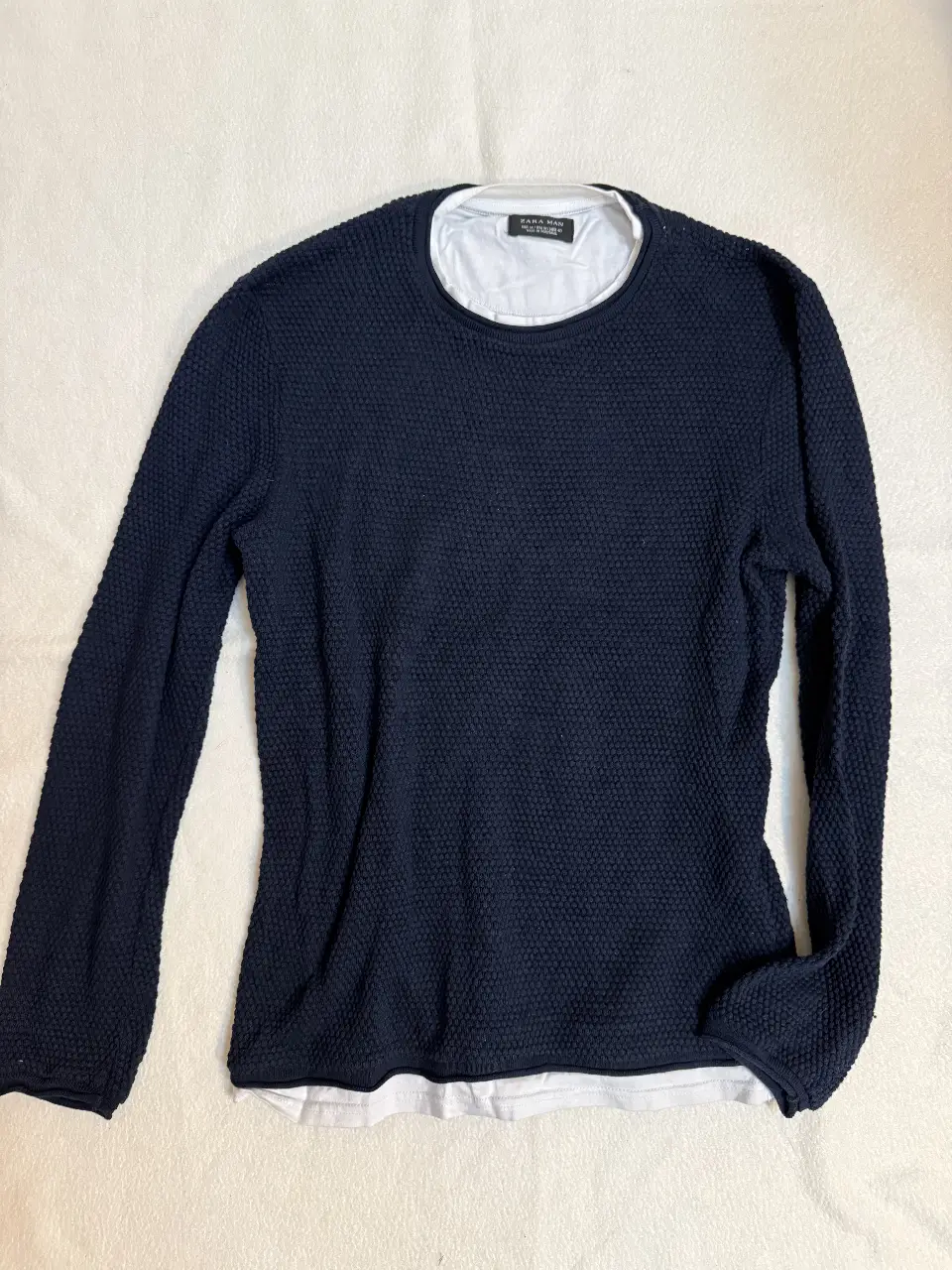 Sweater de hombre azul marino con textura, cuello redondo y manga larga. Incluye una remera blanca de cuello redondo debajo pero solo las partes visibles, creando un efecto de capas. Ideal para un look casual y moderno. 