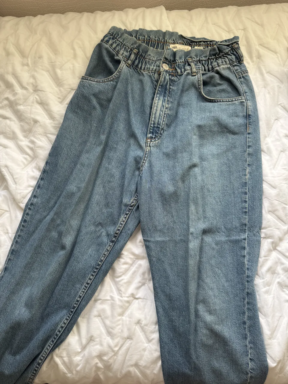 Jeans de tiro alto con cintura elastizada y detalles de frunces. Corte relajado y moderno, perfectos para un look casual y cómodo. Lavado clásico en tono denim.