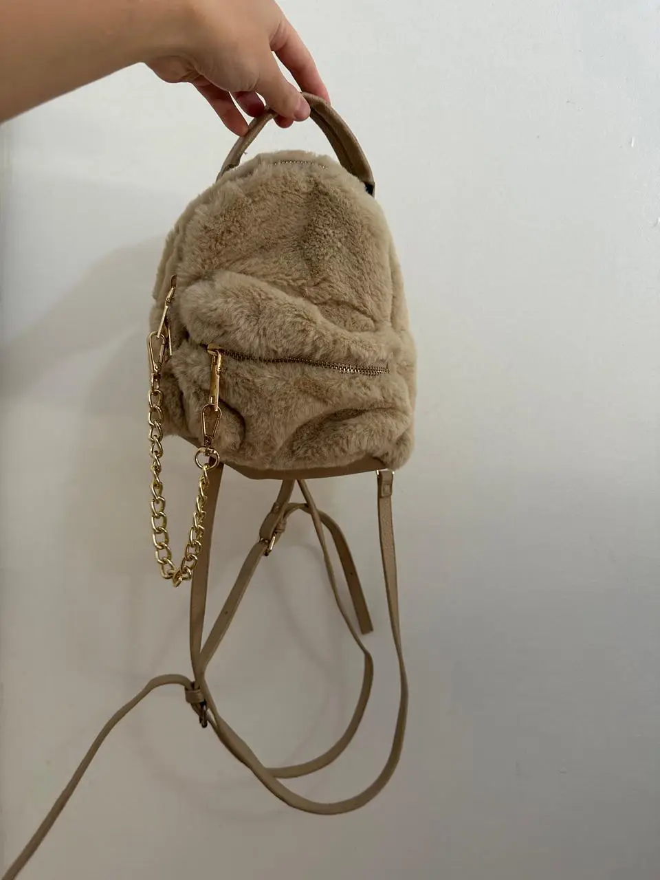 Mochila mini de peluche color marrón. Tiene detalles dorados como la cadena y los cierres. Ideal para un look canchero y cómodo.