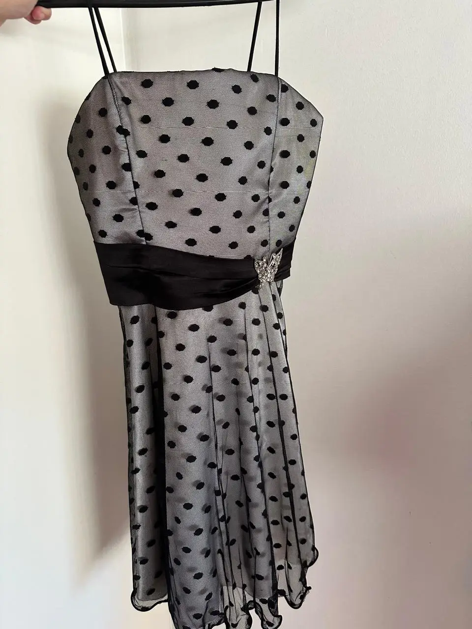 Vestido mini de fiesta con diseño de lunares. Cuenta con detalles de encaje y un cinturón negro que acentúa la cintura. Incluye un broche decorativo.
